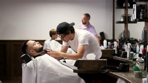 Peluquero en gorra negra clipping clientes barba en barbería . — Vídeo de stock