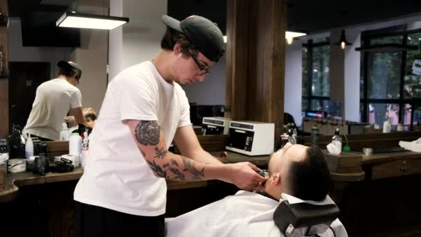 Peluquero en gorra negra clipping clientes barba en barbería . — Vídeo de stock