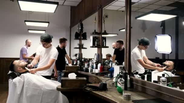 Friseur mit schwarzer Mütze schneidet Kunden Bart im Friseurladen. — Stockvideo