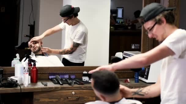 Estilista em camiseta branca e cliente barbudo na barbearia — Vídeo de Stock