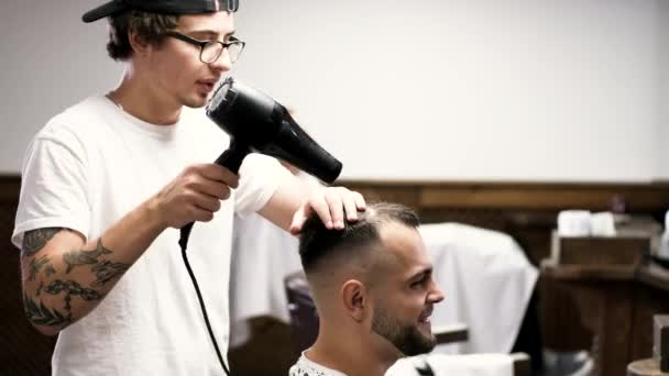 Peluquería seca el cabello de los clientes con secador de pelo en la barbería — Vídeos de Stock
