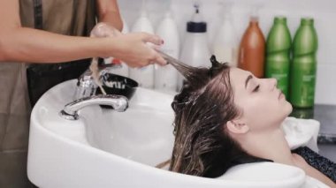 Kuaför kadın saçını beyaz lavaboda şampuanla yıkıyor.