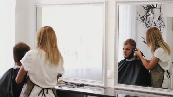 Стилист делает стильную стрижку для клиента в парикмахерской — стоковое видео
