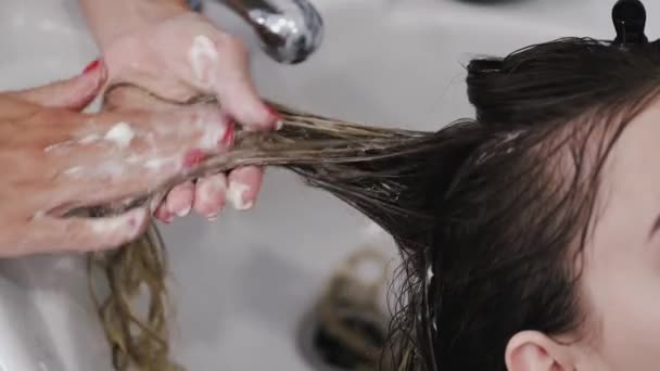 Парикмахер стирает женские волосы с шампунем в белой раковине — стоковое видео