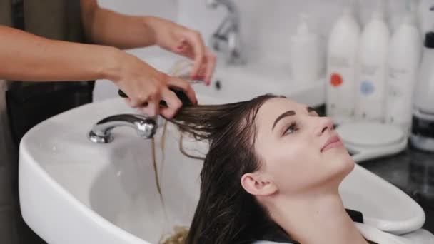 Hairdresser washing womans hair with shampoo in white sink — Stock Video