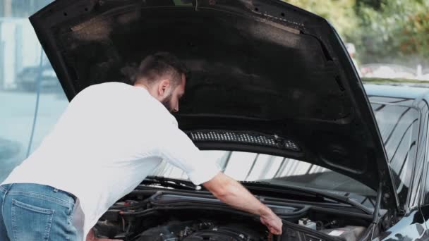 Man met baard in wit shirt repareren auto buiten — Stockvideo