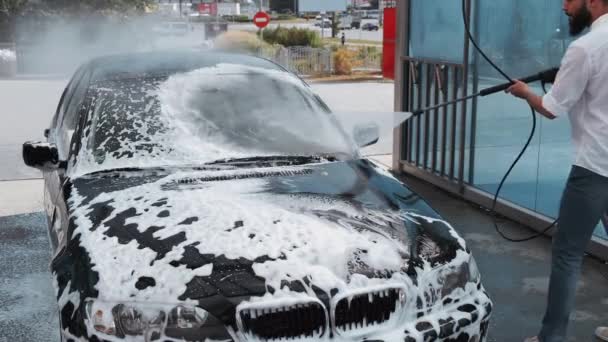 Водитель моет черный автомобиль на автомойке — стоковое видео