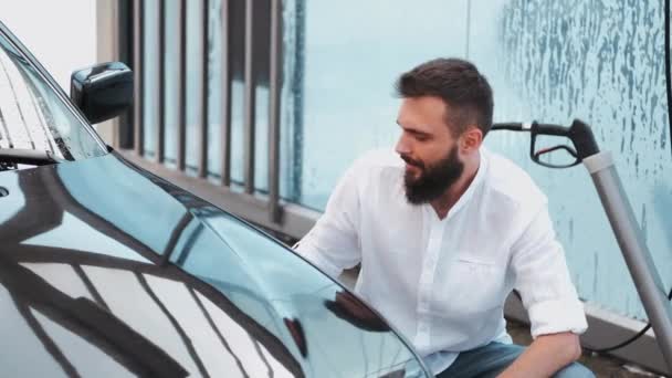 Mężczyzna w koszuli myje czarny samochód w myjni samochodowej — Wideo stockowe