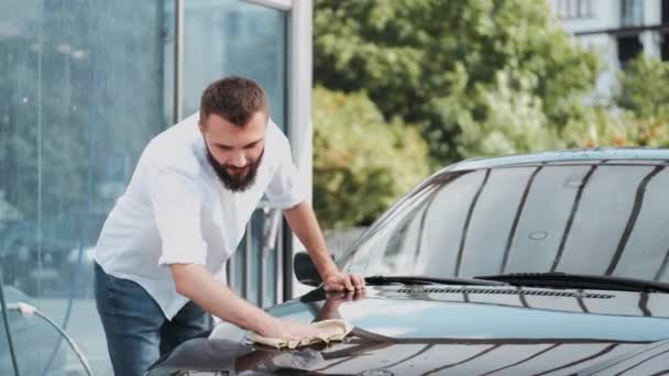 Бородатий чоловік миє машину з тканиною на автомийці — стокове відео