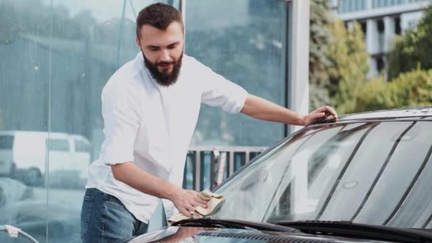 Бородатый мужчина моет машину с тряпкой на автомойке — стоковое видео