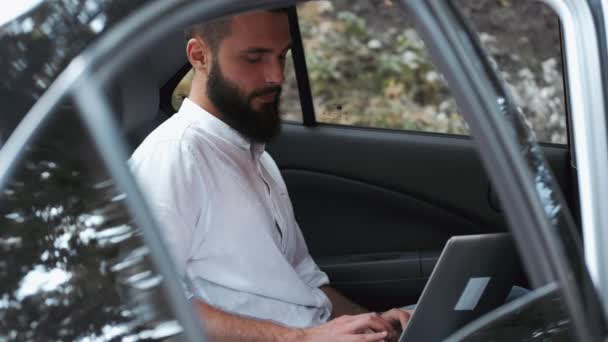 Чоловік у сорочці сидить на задньому сидінні з ноутбуком — стокове відео