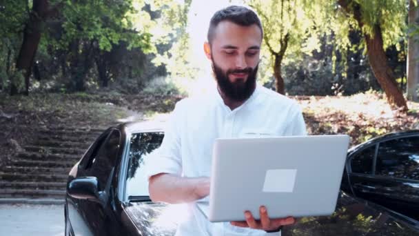 Barbudo hombre en camisa usando portátil cerca de coche — Vídeos de Stock