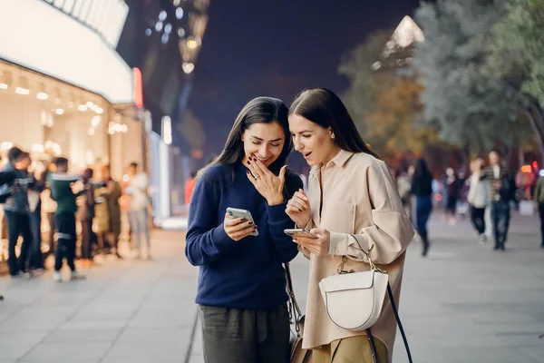 Две девушки, пользующиеся мобильным телефоном во время ночного путешествия по новому городу — стоковое фото