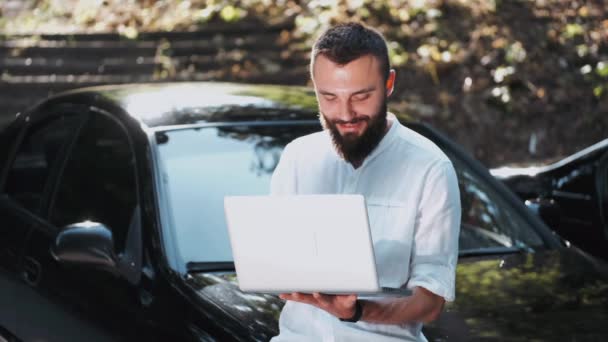 Γενειοφόρος άνδρας σε πουκάμισο χρησιμοποιώντας φορητό υπολογιστή κοντά στο αυτοκίνητο — Αρχείο Βίντεο