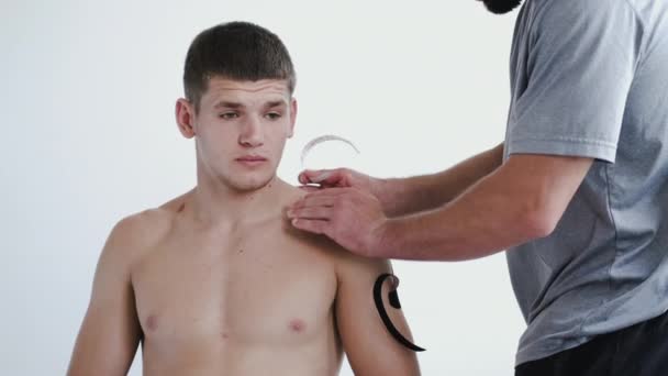 Osteopata provádějící kineziologické pásky na rameni pacientů na klinice — Stock video