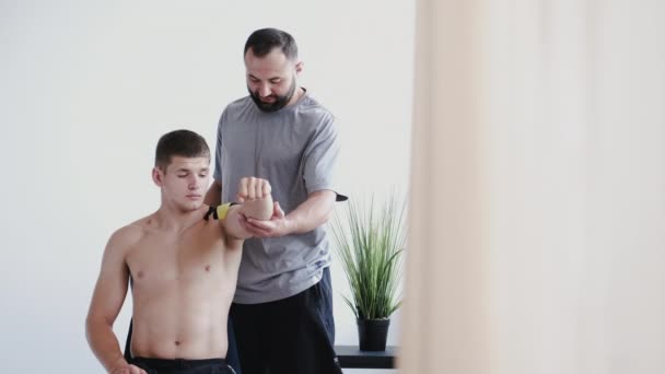 Fisioterapeuta colocando fita cinesiologia no ombro do atleta na clínica — Vídeo de Stock