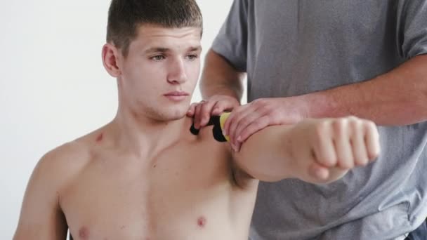 Physiotherapeut legt Kinesiologie-Band auf Schulter des Athleten in Klinik — Stockvideo