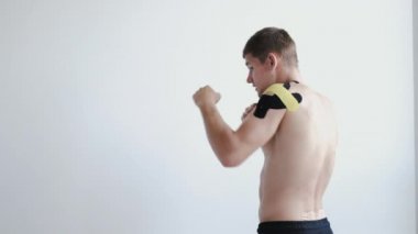 Klinikte omzunda kineziyoloji bandı olan tişörtsüz bir sporcu.