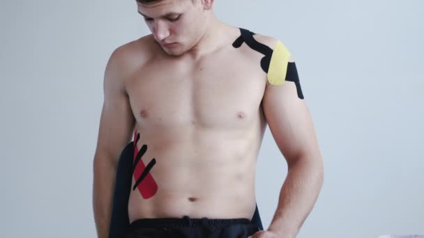 Shirtless athlete with kinesiology tape on shoulder in clinic — Stock Video