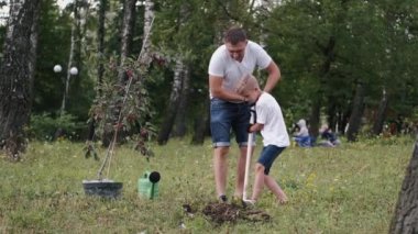 The European boy and dad are digging a hole for a tree