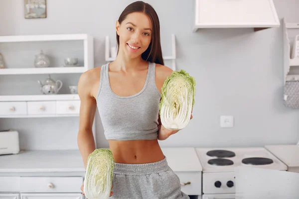 Schöne und sportliche Mädchen in einer Küche mit Gemüse — Stockfoto