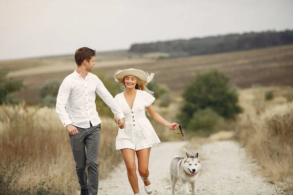 Casal em um campo de outono brincando com um cão — Fotografia de Stock