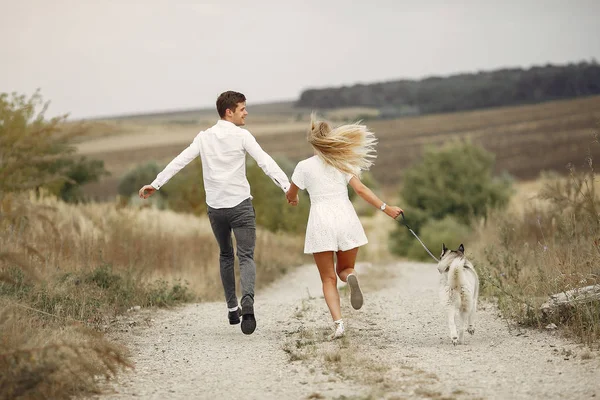 Casal em um campo de outono brincando com um cão — Fotografia de Stock