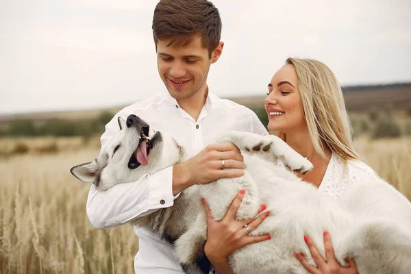 Casal em um campo de outono brincando com um cão — Fotografia de Stock