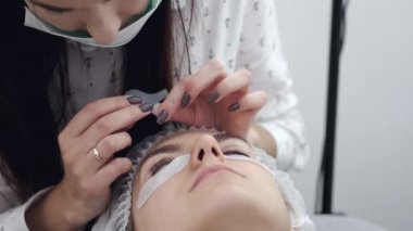 Kirpik ustası bir aletle göz kirpiklerini fırçalıyor.