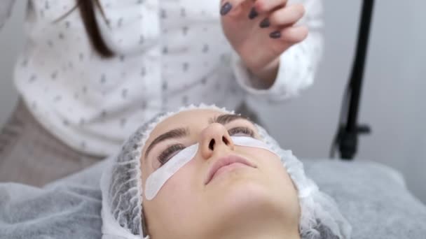 Der Ästhetiker trägt den Wimpernkleber gleichmäßig auf die Wimpern auf — Stockvideo