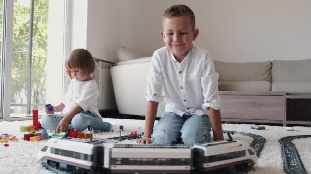 Двое детей вместе играют в игрушечную железную дорогу дома — стоковое видео