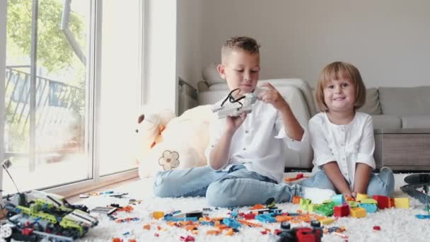 Çocuklar halıda oturup evde lego tuğlalarıyla oynuyorlar. — Stok video