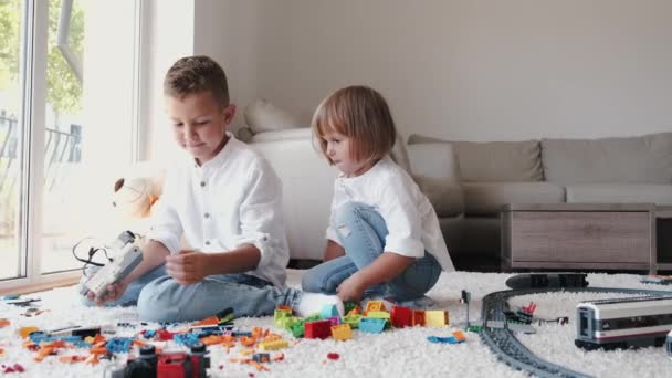 Niños sentados en la alfombra jugando con ladrillos lego en casa — Vídeo de stock