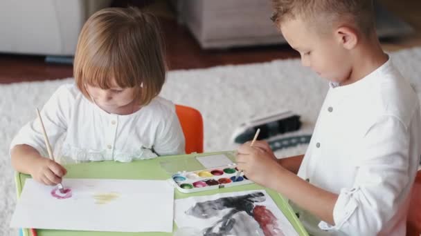 Erkek ve kız kardeş evde boya fırçalarını tutarak birlikte çiziyorlar. — Stok video