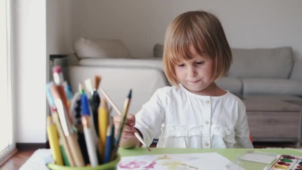 Портрет маленької дівчинки, що тримає пензлик і малює вдома — стокове відео