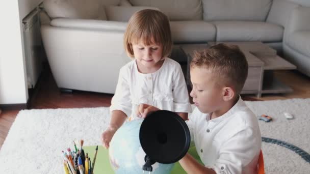 Irmão e irmã explorando o mundo com globo juntos em casa — Vídeo de Stock