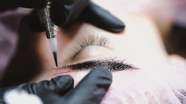 Der Schönheitsmeister in Gummihandschuhen färbt einem Kunden mit der Microblading-Technik die Augenbrauen ab — Stockvideo