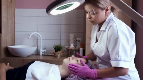 Kosmetolog stosujący krem do twarzy i masaży kobieta w salonie — Wideo stockowe