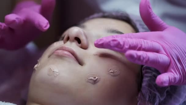 Косметолог наносить крем на обличчя і масажує жінку в салоні — стокове відео
