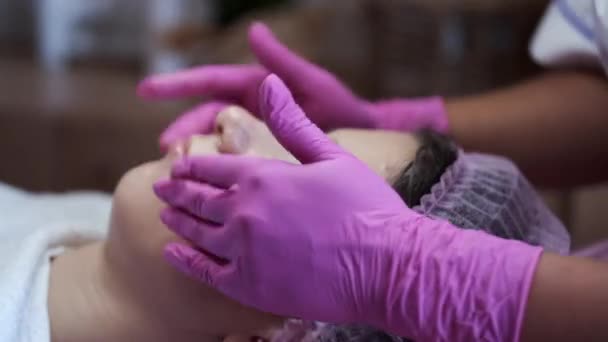 Cosmetologo che applica la crema a faccia e massaggia la donna in salone — Video Stock