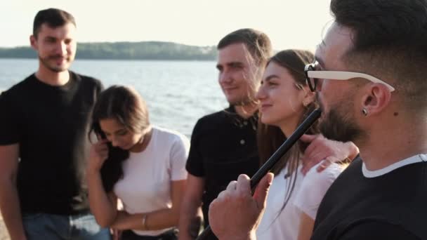 Amigos gastando tempo fumando shisha perto do lago no verão — Vídeo de Stock