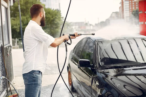 Hombre guapo en una camisa blanca lavando su coche — Foto de Stock