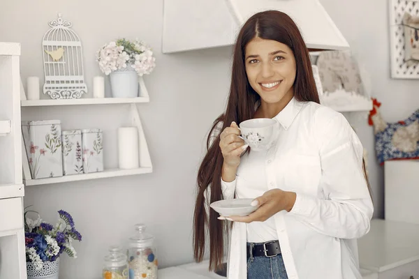 Žena v bílé košili stojí v kuchyni a popíjí kávu — Stock fotografie