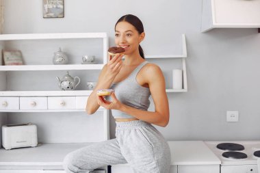 Güzel bir kız mutfakta donutla duruyor.