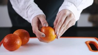 The mandarin fruit is being peeled over a cutting board