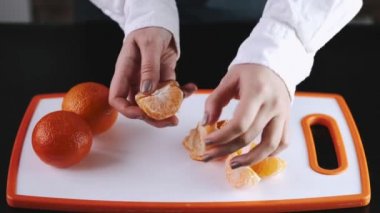 The mandarin fruit is being peeled over a cutting board