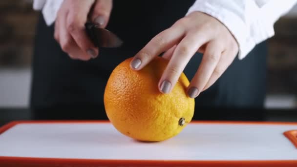 La gran naranja está siendo cortada en una tabla de cortar — Vídeos de Stock