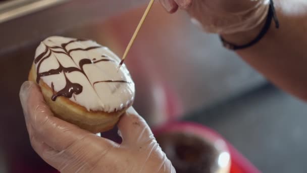 The baker is decorating a donut with a topping — Stockvideo