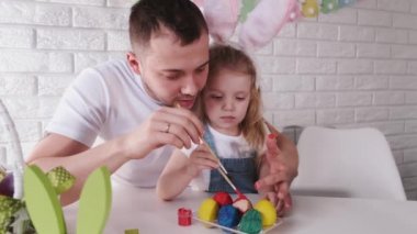 Baba ve küçük kızı paskalya yumurtalarını fırçayla renklendiriyorlar.