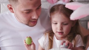 Baba ve küçük kızı paskalya yumurtalarını fırçayla renklendiriyorlar.